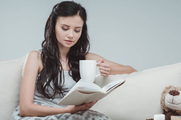istock Attractive young woman drinking tea and reading book at home 802337542