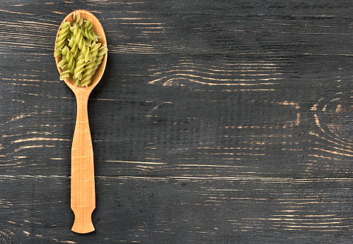 Green fusilli pasta in spoon on wooden background, top view
