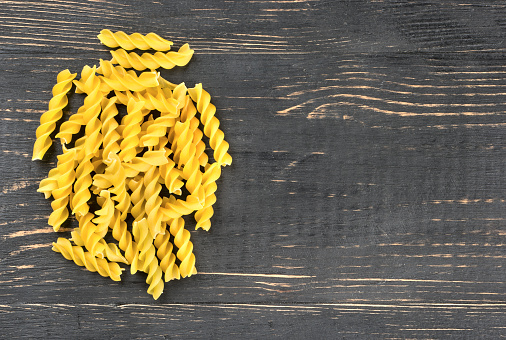 Bunch of raw pasta fusilli on an empty wooden background, top view