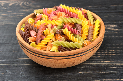 Colored pasta fusilli in a bowl on wooden background