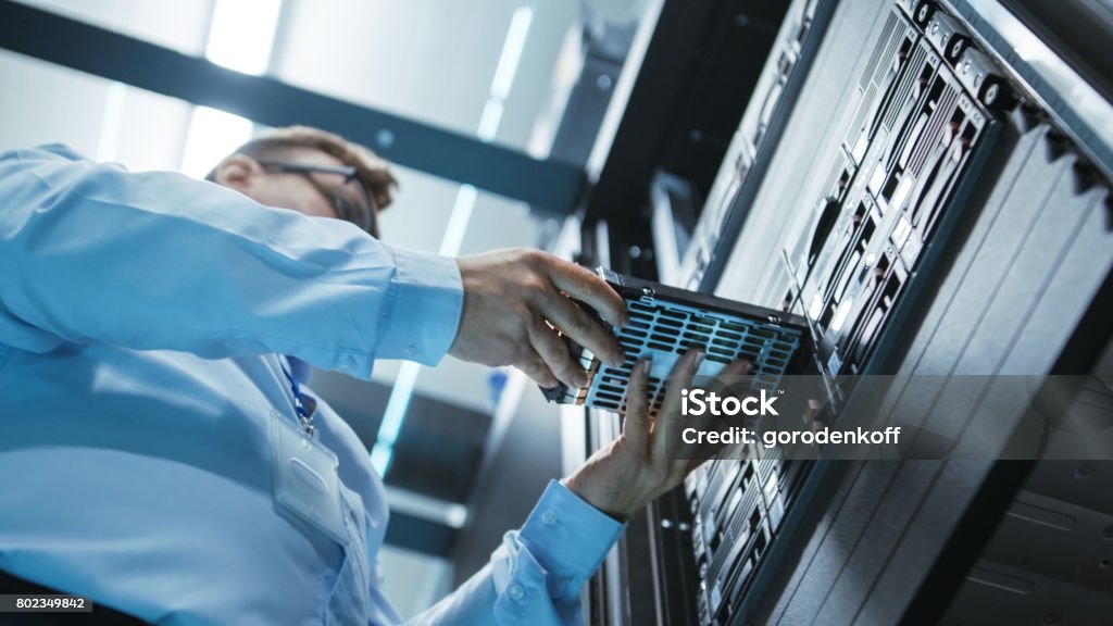 Long Angle Shot In Fully Working Data Center of IT Engineer Installing Hard Drive into Server Rack. Detailed and Technically Accurate Footage. Network Server Stock Photo