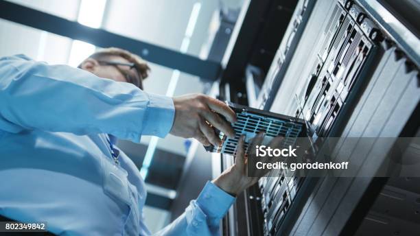 Long Angle Shot In Fully Working Data Center Of It Engineer Installing Hard Drive Into Server Rack Detailed And Technically Accurate Footage Stock Photo - Download Image Now