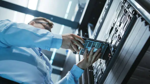 Photo of Long Angle Shot In Fully Working Data Center of IT Engineer Installing Hard Drive into Server Rack. Detailed and Technically Accurate Footage.