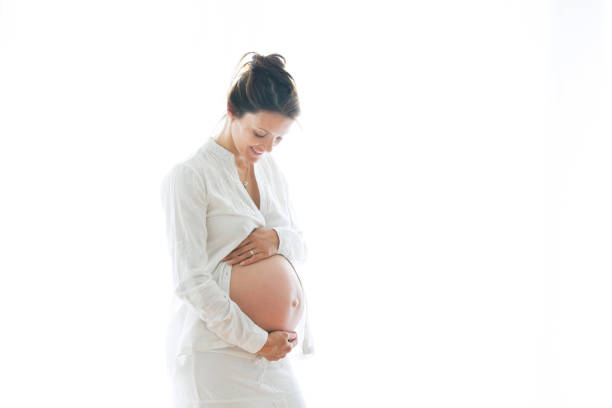 portrait de jeune femme enceinte attrayante, debout près de la fenêtre, - abdomen adult affectionate baby photos et images de collection