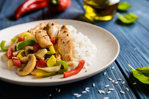 Fried chicken breasts pieces served with rice and steamed bell pepper, leek, mushrooms and garlic