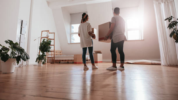 Young couple moving in new house Full length rear view shot of young couple carrying cardboard box at new home. Young man and woman holding boxes and moving in new house. living space
