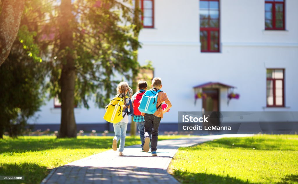 Children with rucksacks running in the park near school Children with rucksacks running in the park near school. Pupils with books and backpacks outdoors Education Stock Photo