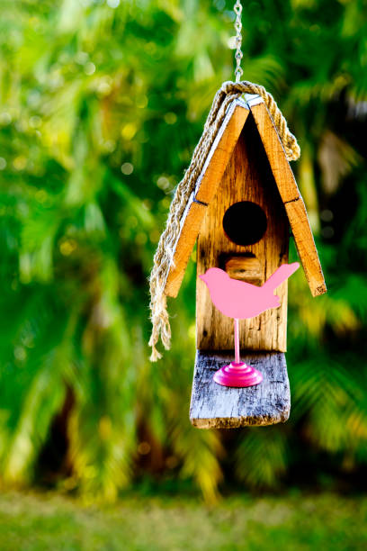 istock Simple rustic wooden birdhouse hanging against greenery background with pink bird figure 802410560