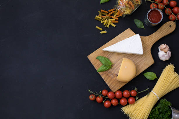 Food frame. Pasta ingredients. Cherry-tomatoes, spaghetti pasta, garlic, basil , cheese and spices on dark grunge backdrop, copy space, top view