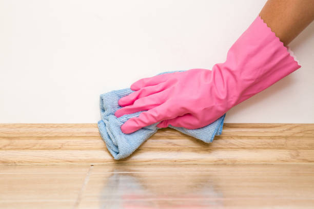 istock Hand in rubber protective glove cleaning baseboard on the floor from dust with rag at the wall. Early spring cleaning or regular clean up. Maid cleans house. 802416630