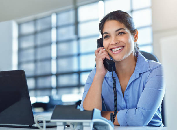 Who can I connect you with? Shot of a young businesswoman answering a phone while using her laptop at her desk answering stock pictures, royalty-free photos & images