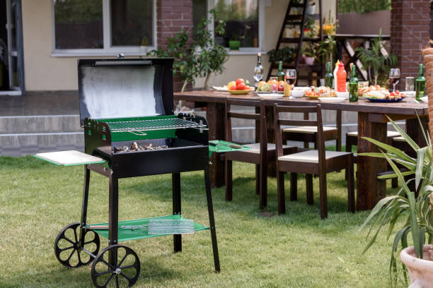 istock Outdoor grill with coals standing on green lawn and served table with dishes and drinks behind 802425442