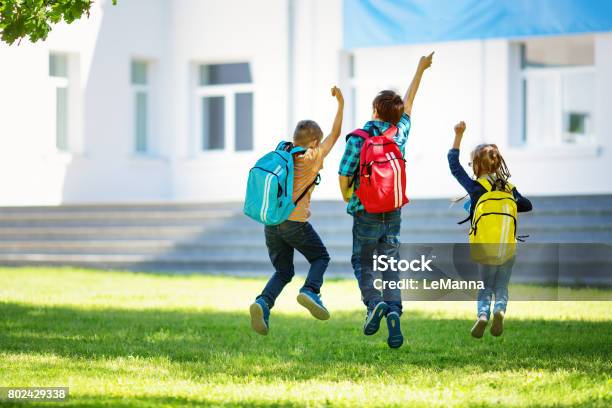 Children With Rucksacks Jumping In The Park Near School Stock Photo - Download Image Now