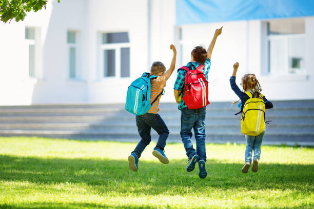 dzieci z plecakami skaczącymi w parku w pobliżu szkoły - school classroom child back to school zdjęcia i obrazy z banku zdjęć