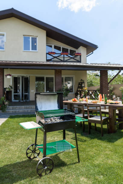 istock Outdoor grill with coals standing on green lawn and served table with dishes and drinks behind 802436654