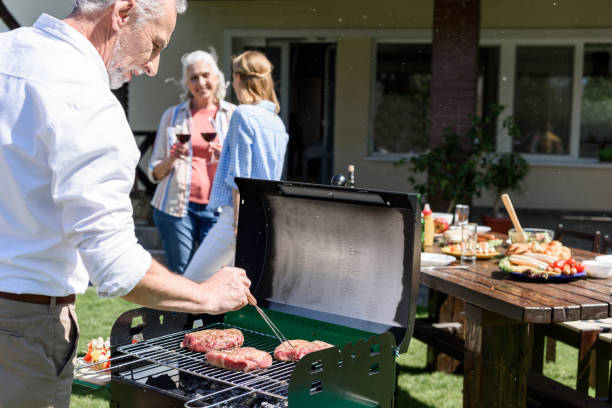 istock Smiling senior man making barbecue at outdoor grill while women drinking wine behind 802439708