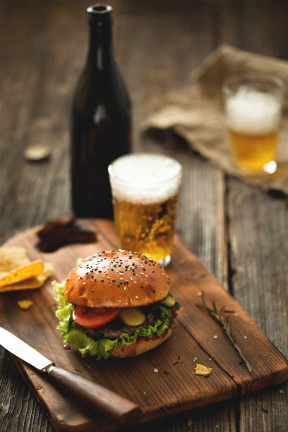 Burger with salad and glass of beer on wooden table. - fotografia de stock