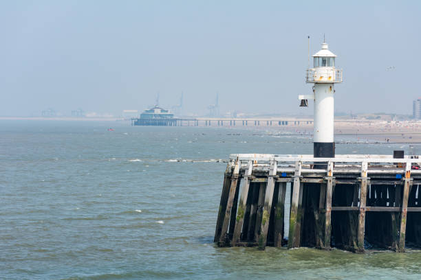 Lighthouse on old harbor jetty of Blankenberge harbor with pier in the backdrop
