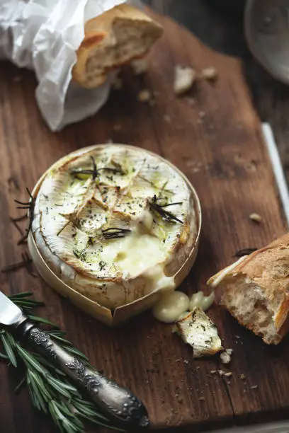 Baked camembert in oven with herbs on a wooden table.
