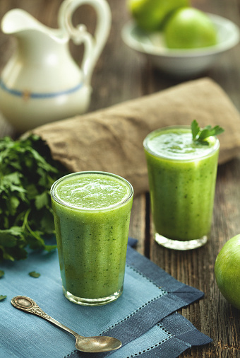 Green smoothie healthy drink in faceted glass on wooden table.