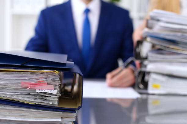 istock Binders with papers are waiting to be processed with businessman and secretary back in blur. Accounting planning budget, audit, insurance  and business concept 802459048