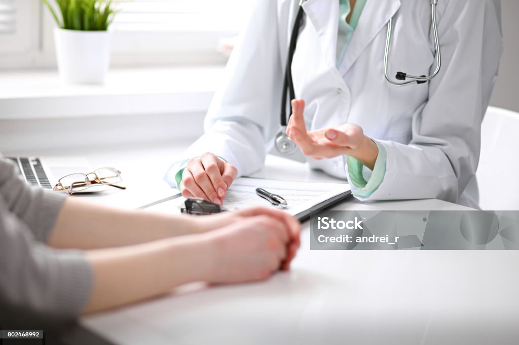 Cerca de doctor y el paciente sentado en el escritorio cerca de la ventana en el hospital - Foto de stock de Doctor libre de derechos