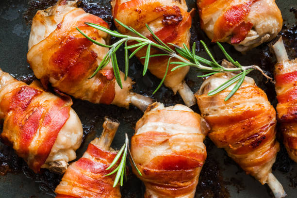 istock Oven roasted bacon wrapped chicken drumsticks in a black baking pan, top view. 802472832