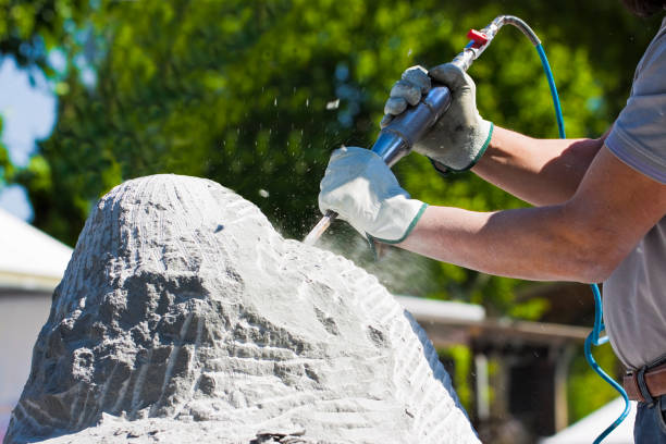 Young man at work with compressed air chisel and protective gloves to carving a stone block