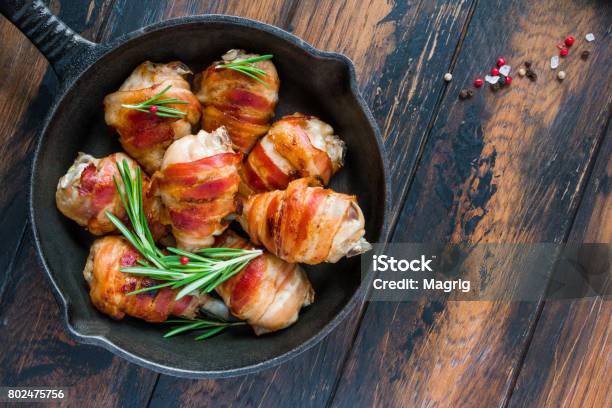 Tocino Envuelto Contramuslos De Pollo En Una Sartén De Hierro Fundida Negro Sobre La Mesa Rústica De Madera Vista Superior Foto de stock y más banco de imágenes de Tocino ahumado