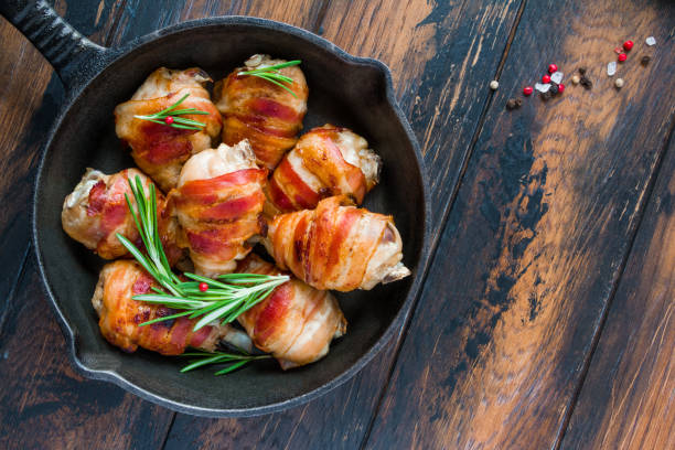 Bacon wrapped chicken drumsticks in a black cast-iron skillet on the wooden rustic table, top view. Bacon wrapped chicken drumsticks in a black cast-iron skillet on the wooden rustic table, top view. bacon wrapped stock pictures, royalty-free photos & images