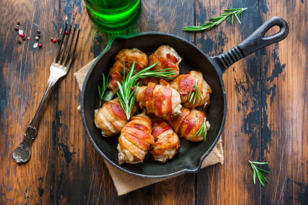 istock Oven roasted bacon wrapped chicken drumsticks in a black baking pan on the wooden rustic table, top view. 802476320
