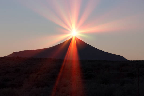 Sun with flare and silhouette of hill peak stock photo
