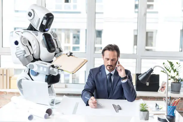 Modern way of life. Concentrated serious businessman is holding pencil and talking on smartphone while his assistant robot is passing him envelopes