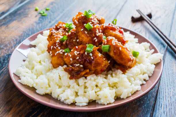 pollo al sesamo croccante, filetti di petto tritati, con una salsa asiatica dolce appiccicosa e riso bollito bianco su un piatto su un tavolo di legno. - sesamo foto e immagini stock