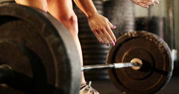Young Woman in Gym Young woman standing by barbells before lifting weight. crossfit chalk weightlifting weight training stock pictures, royalty-free photos & images