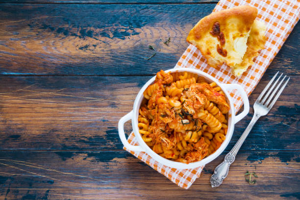 fusilli pasta with chicken. cooked in spicy sauce from tomatoes, onion, garlic, dried oregano and thyme, paprika and olive oil. bread, white bowl and casserole on wooden brown rustic table. top view. - oregano freshness herb brown imagens e fotografias de stock