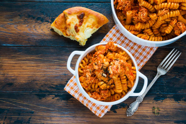 fusilli pasta with chicken. cooked in spicy sauce from tomatoes, onion, garlic, dried oregano and thyme, paprika and olive oil. bread, white bowl and casserole on wooden brown rustic table. top view. - oregano freshness herb brown imagens e fotografias de stock