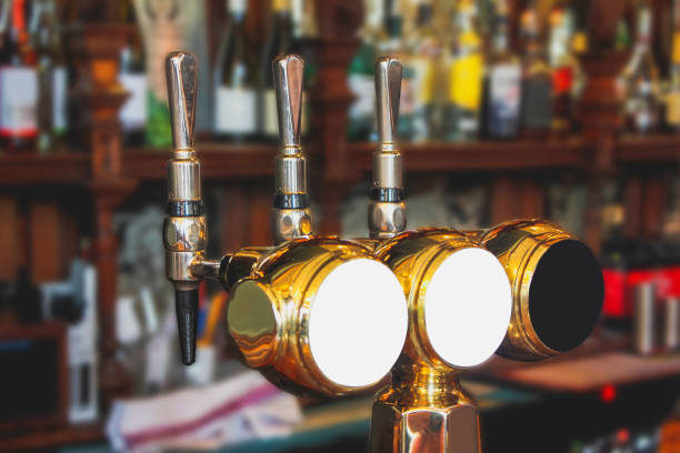 Variation beer tap in pub Close up beer tap in a row, above bar with blurred variation alcohol bottle in the background. beer pump stock pictures, royalty-free photos & images