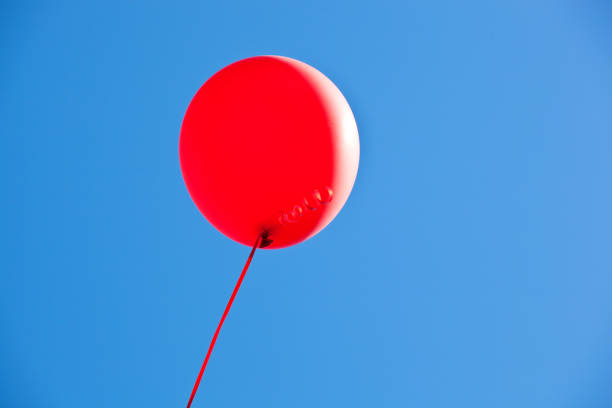 istock Red Balloons Flying in Bright Blue Sky 802558248