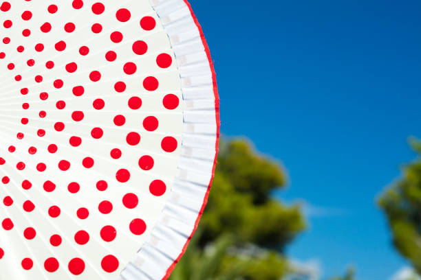 White Hand-held fan (or spanish fan) with red dots and blue sky at the background