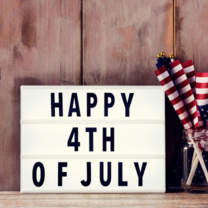 a lightbox with the text happy 4th of july and some american flags on a glass jar, on a rustic wooden background