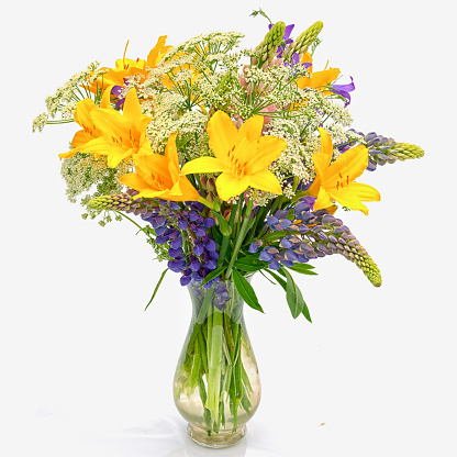 bouquet od wild flowers: achillea millefolium, day lily and lupine in a transparent glass vase isolated on white background