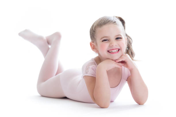 Cute elementary age Caucasian ballerina smiles while lying on the floor in a dance studio.