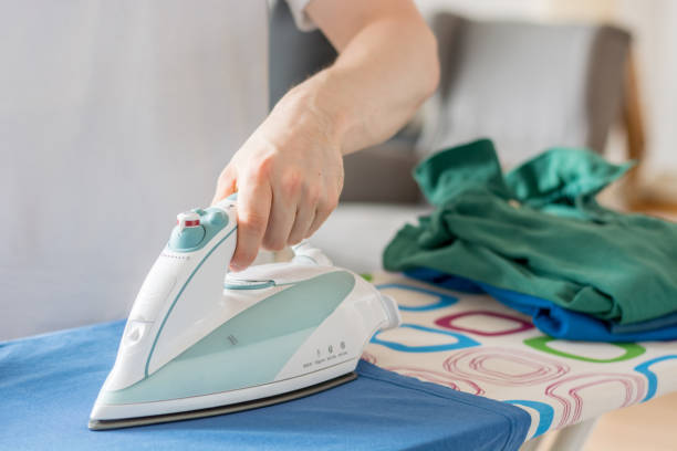 istock An iron on an ironing board with a blue shirt close up from the side with a stack of laundry 802592820
