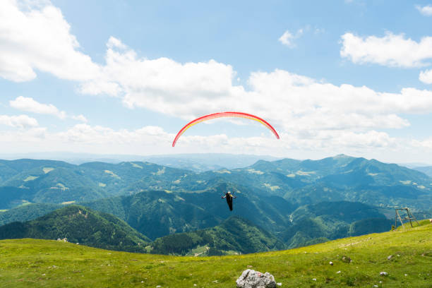 One Paraglider with red parachut flying over green hils against blue sky.