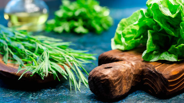 Fresh herbs variety Fresh leaf salad on cutting board and tarragon on wooden plate. Olive oil in cruet. Spotty blue background. Close up tarragon cutting board vegetable herb stock pictures, royalty-free photos & images