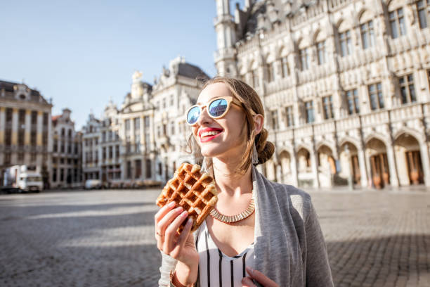 Woman with belgian waffle outdoors Young woman walking with waffle a traditional belgian pastry food in the center of Brussels city during the morning brussels capital region photos stock pictures, royalty-free photos & images