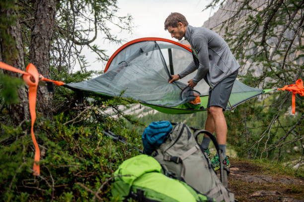 istock Man preparing hanging tent camping mosquito net in overcast day. Group of friends people summer adventure journey in mountain nature outdoors. Travel exploring Alps, Dolomites, Italy 802605708