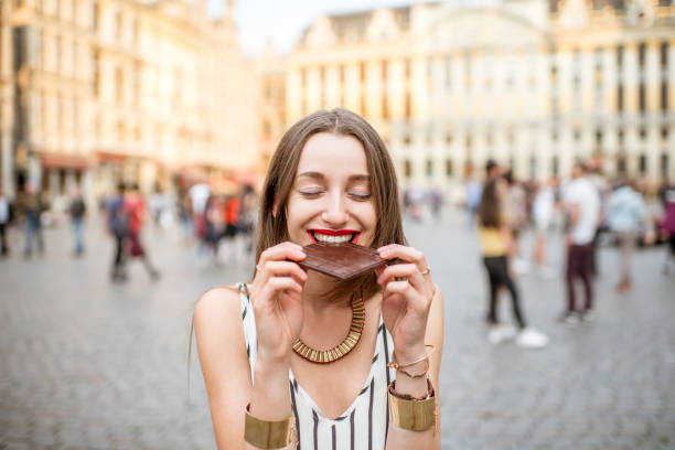 Woman with chocolate outdoors in Brussels Young and happy woman with dark chocolate bar standing outdoors on the Grand place in Brussels in Belgium. Belgium is famous of its chocolate city of brussels stock pictures, royalty-free photos & images