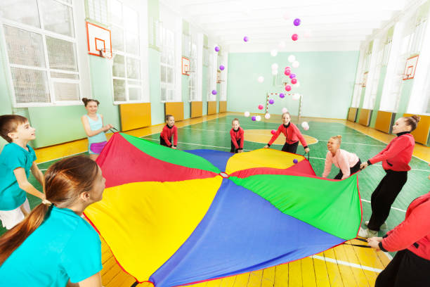 niños felices jugando juego de paracaídas en gimnasio - bouncing ball family playing fotografías e imágenes de stock